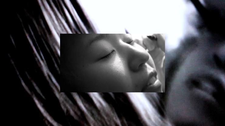 Film still from Lorelei - Persona by Gustavo Gomes. Rectangular image of a woman with eyes closed, layered on a background of black and white light. 