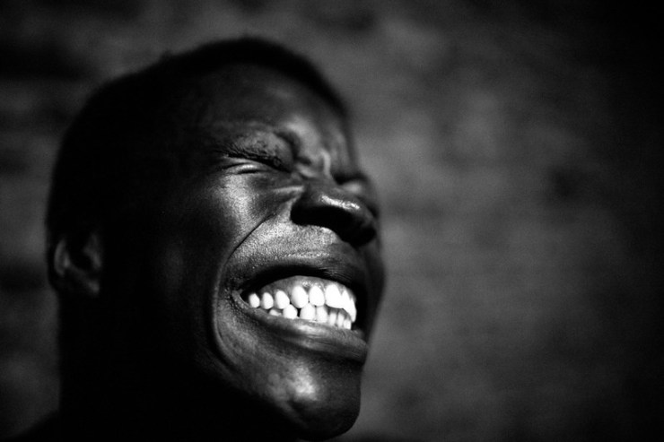 Film still from Observations by David Belotti. Black and white still image of a man, cannot tell if he is smiling or grimacing. 